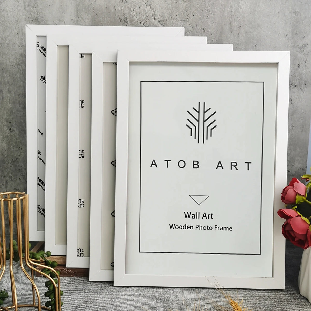 A set of five white wooden photo frames with black line art designs displayed on a gray surface.