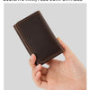 A hand holds a dark brown vintage leather mini card holder used as a cable organizer.