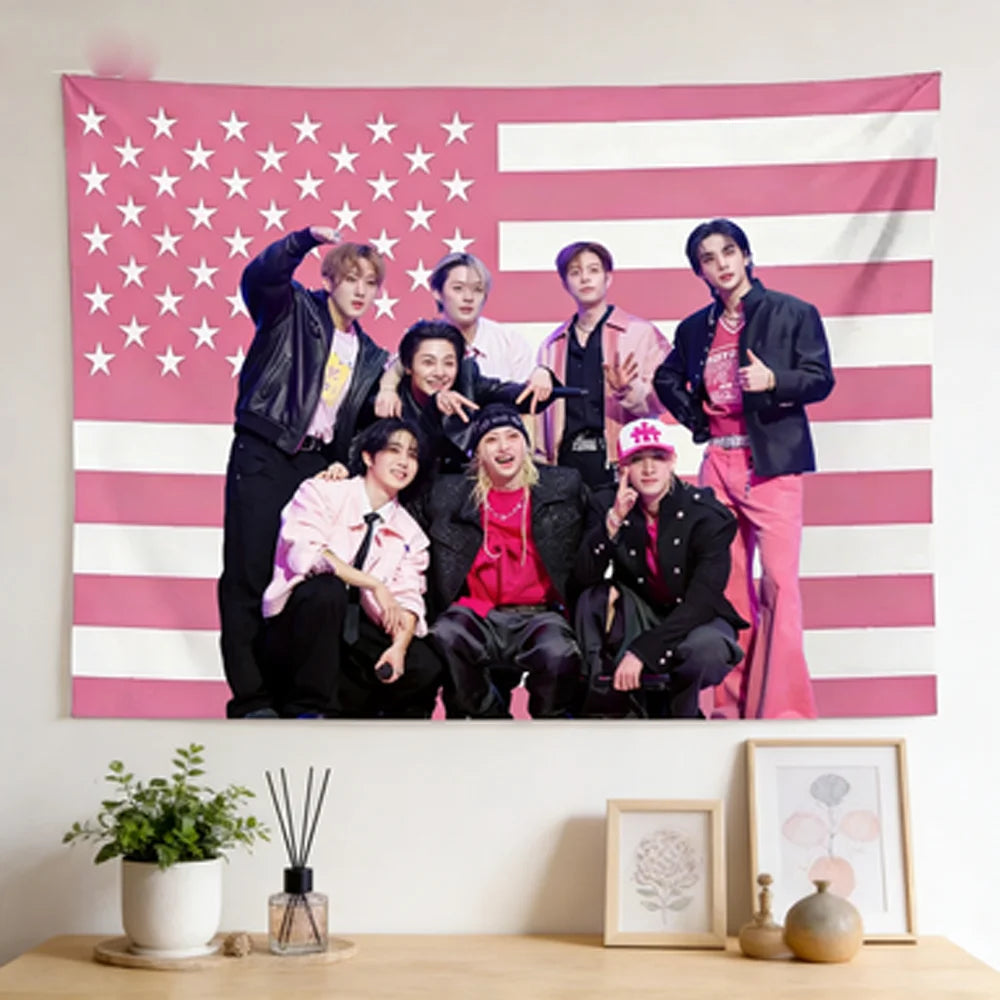 A group of five male Kpop idols posing in front of a pink and white American flag tapestry.