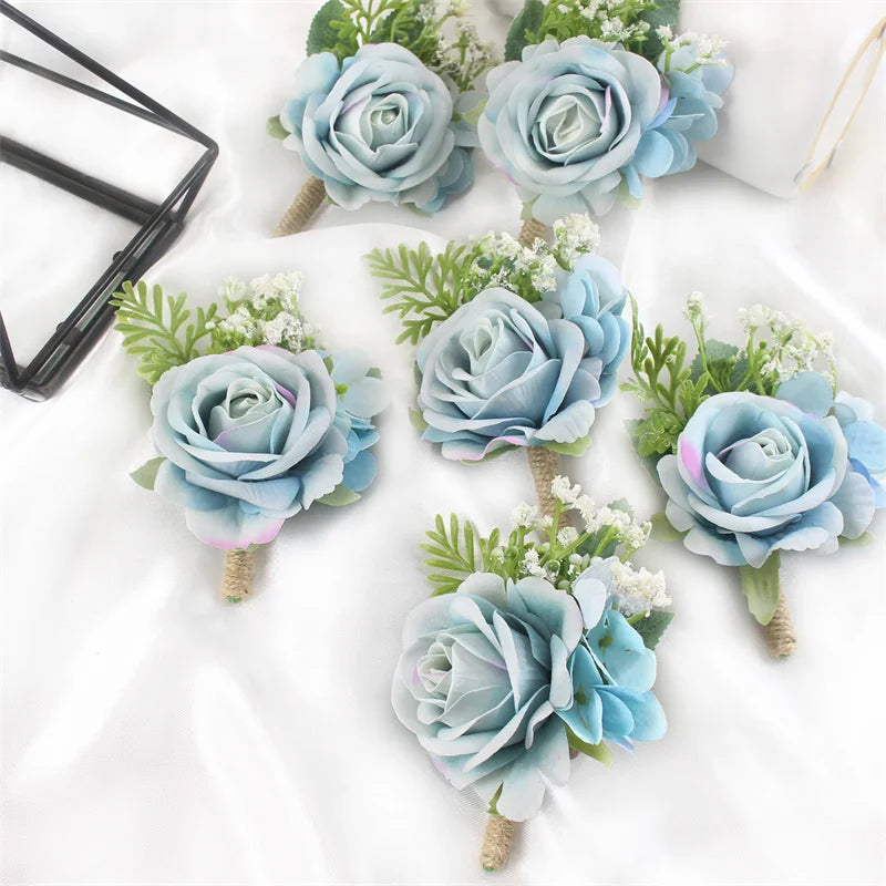 A set of six dusty blue silk rose boutonnières featuring greenery and white filler flowers.