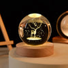 A glass crystal ball with a tree silhouette engraved inside, resting on a wooden base.