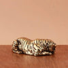 A vintage brass tiger figurine, a miniature animal statue, resting on a wooden surface.