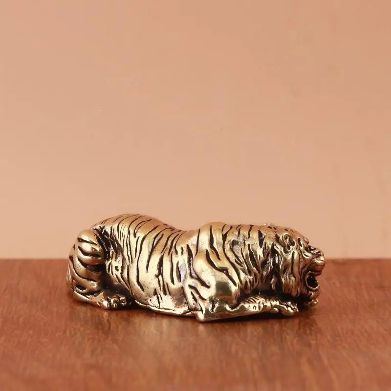 A vintage brass tiger figurine, a miniature animal statue, resting on a wooden surface.
