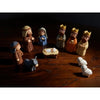 Miniature nativity scene set featuring Mary, Jesus, shepherd, and animal figurines displayed on dark wood.