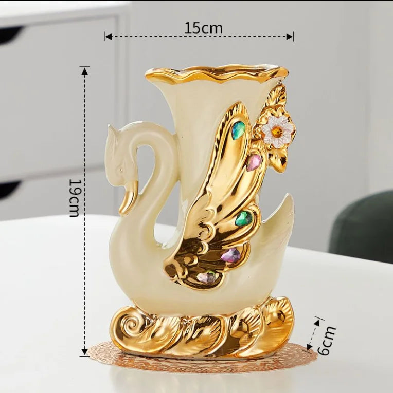 A golden ceramic swan vase with floral accents on a round base, shown against a white background.