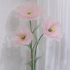 A large artificial silk pink poppy flower displayed on a green stand against a white background.