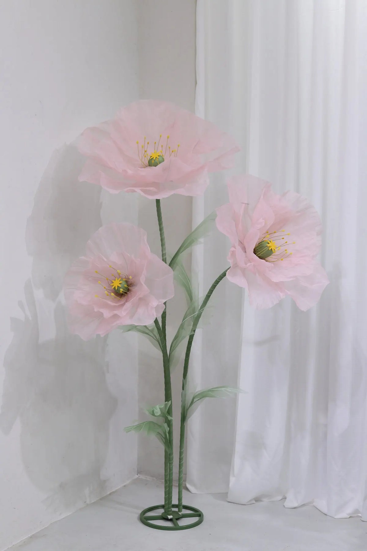 A large artificial silk pink poppy flower displayed on a green stand against a white background.