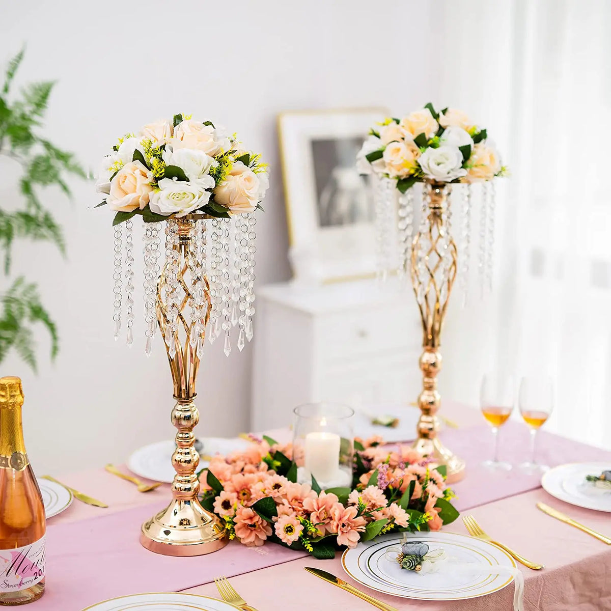 Gold crystal vase set with floral arrangements and cascading crystals on a pink table.