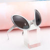 Silver-framed sunglasses with dark lenses displayed on a clear acrylic block.