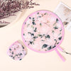 Pink floral patterned portable foldable cooling handheld fan resting on a light background.