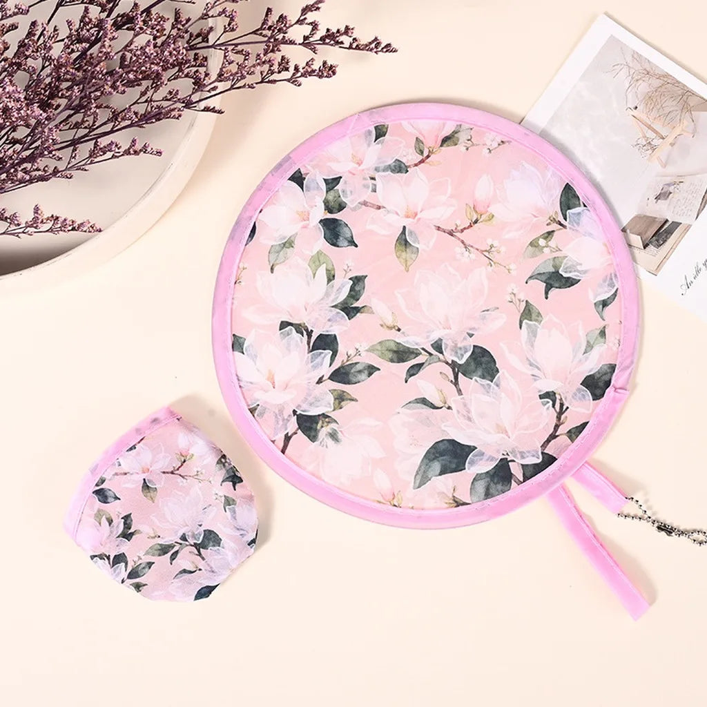 Pink floral patterned portable foldable cooling handheld fan resting on a light background.