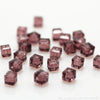 A scattering of square cut glass crystal beads in a dusty rose color on a white background.