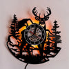 A silhouette of a deer and a moose head with antlers is cut into black wood, backlit by an orange glow.