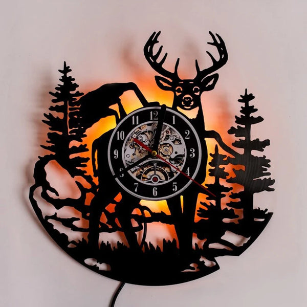 A silhouette of a deer and a moose head with antlers is cut into black wood, backlit by an orange glow.
