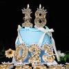 A light blue cake decorated with gold glitter number toppers and candles on a black background.