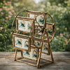 A rotating gold-framed photo display featuring twelve small framed pictures set against a blurred green and pink outdoor back