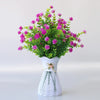 Un bouquet de fleurs artificielles roses et violettes dans un vase en céramique blanche avec une base de fil décorative.