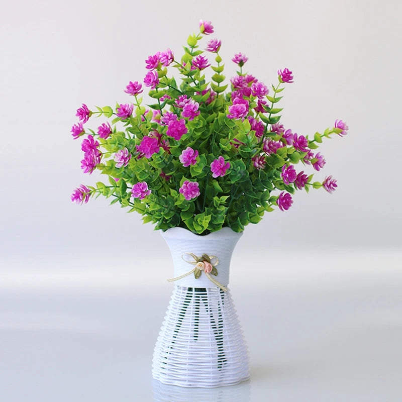 Un bouquet de fleurs artificielles roses et violettes dans un vase en céramique blanche avec une base de fil décorative.