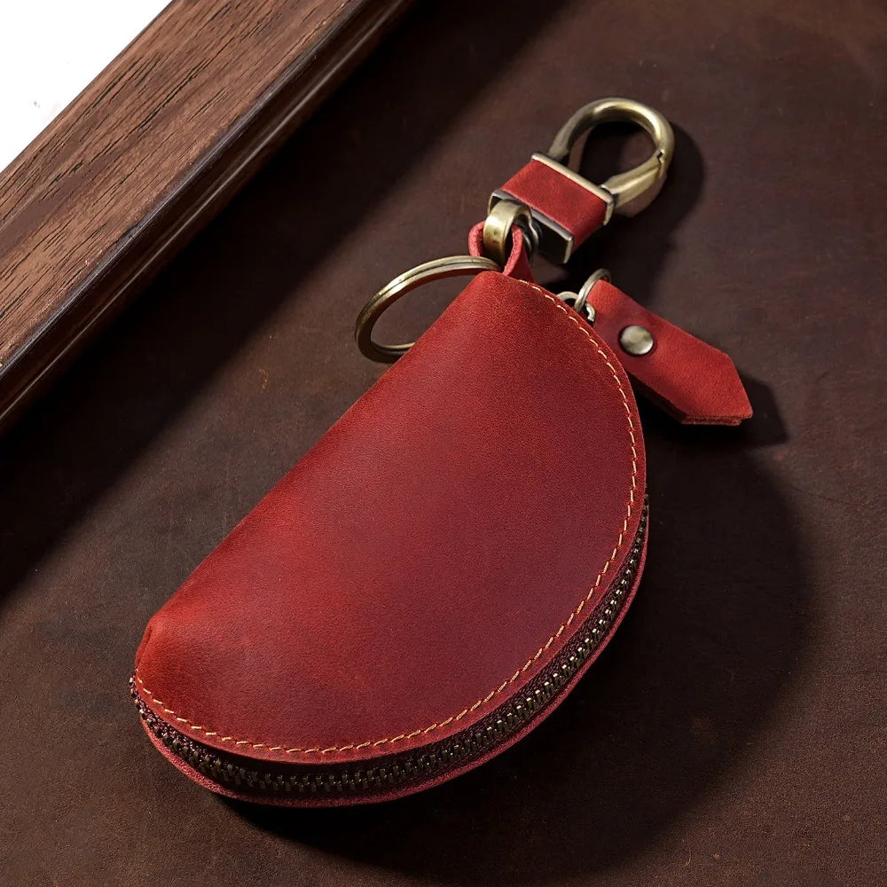 A reddish-brown leather key pouch with a brass carabiner attached, resting on a dark brown surface.