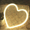 A heart-shaped neon sign with a starry pattern is displayed against a textured wall.