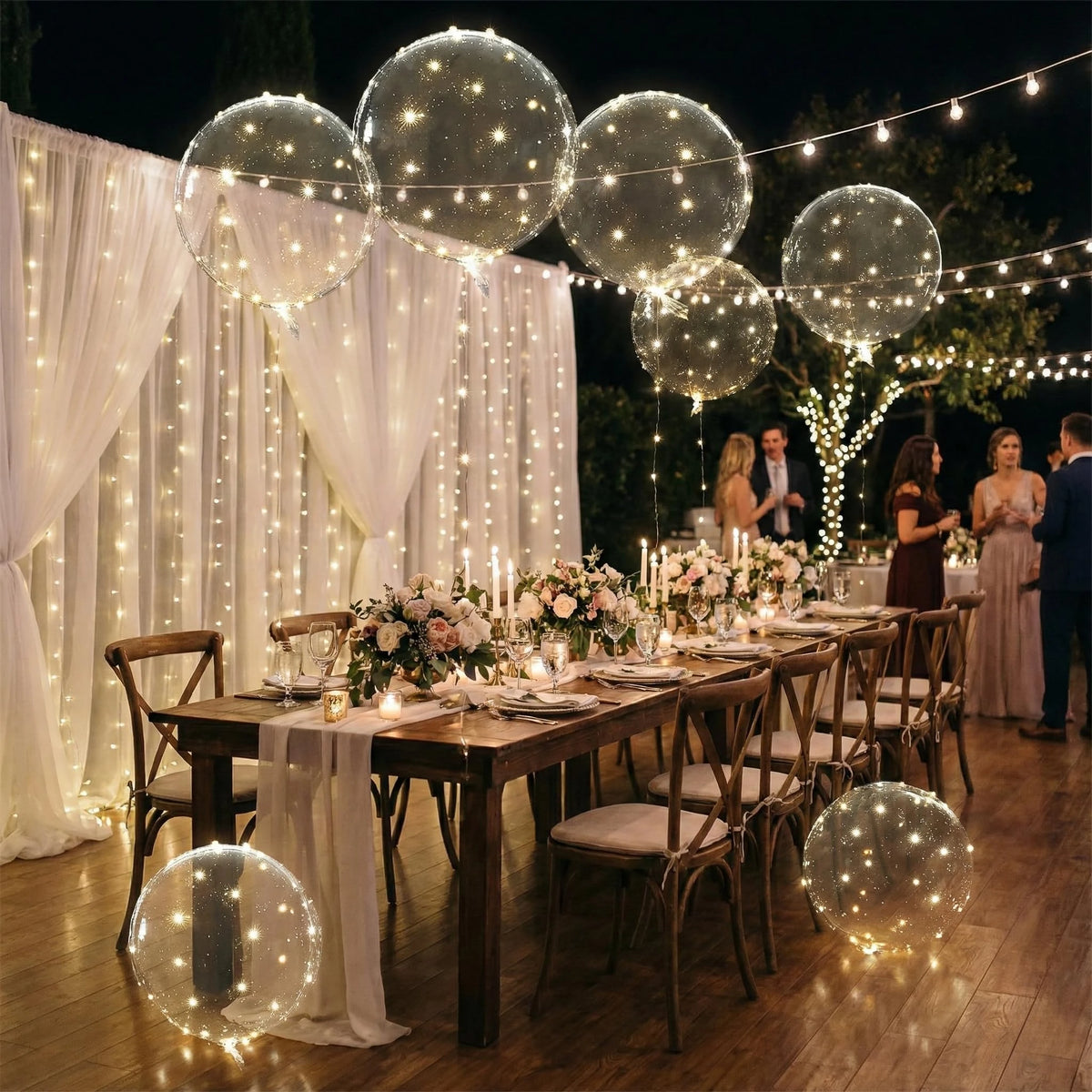 A decorated indoor event featuring wooden tables set for dining surrounded by large illuminated clear balloons and sheer whit