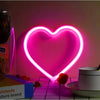 A bright pink heart-shaped LED neon sign is displayed against a pink wall with decorative elements.