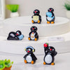 A collection of cute cartoon penguin resin figurines in black and blue sitting on a white surface.