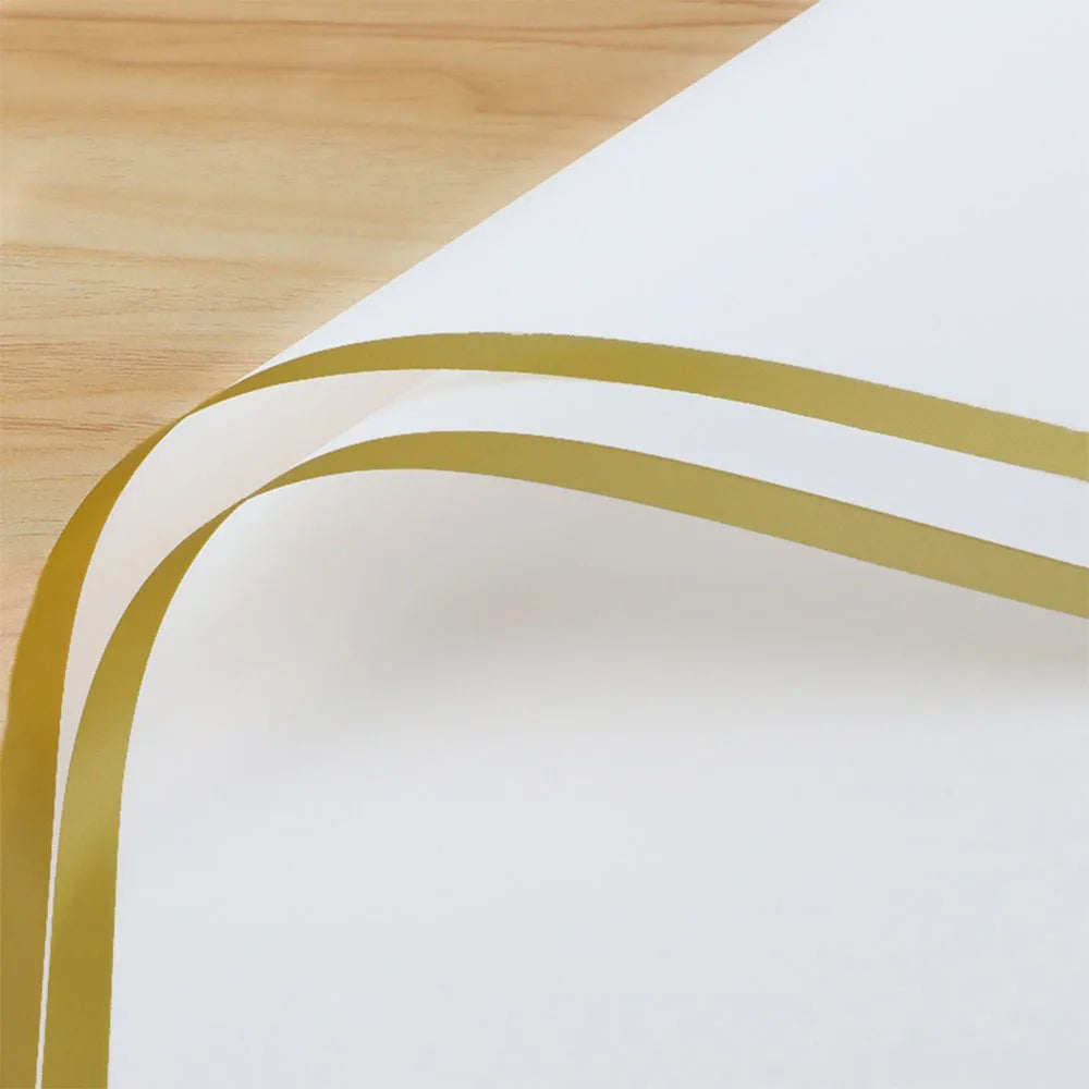 A sheet of white wrapping paper with two gold curved lines on a wooden surface.