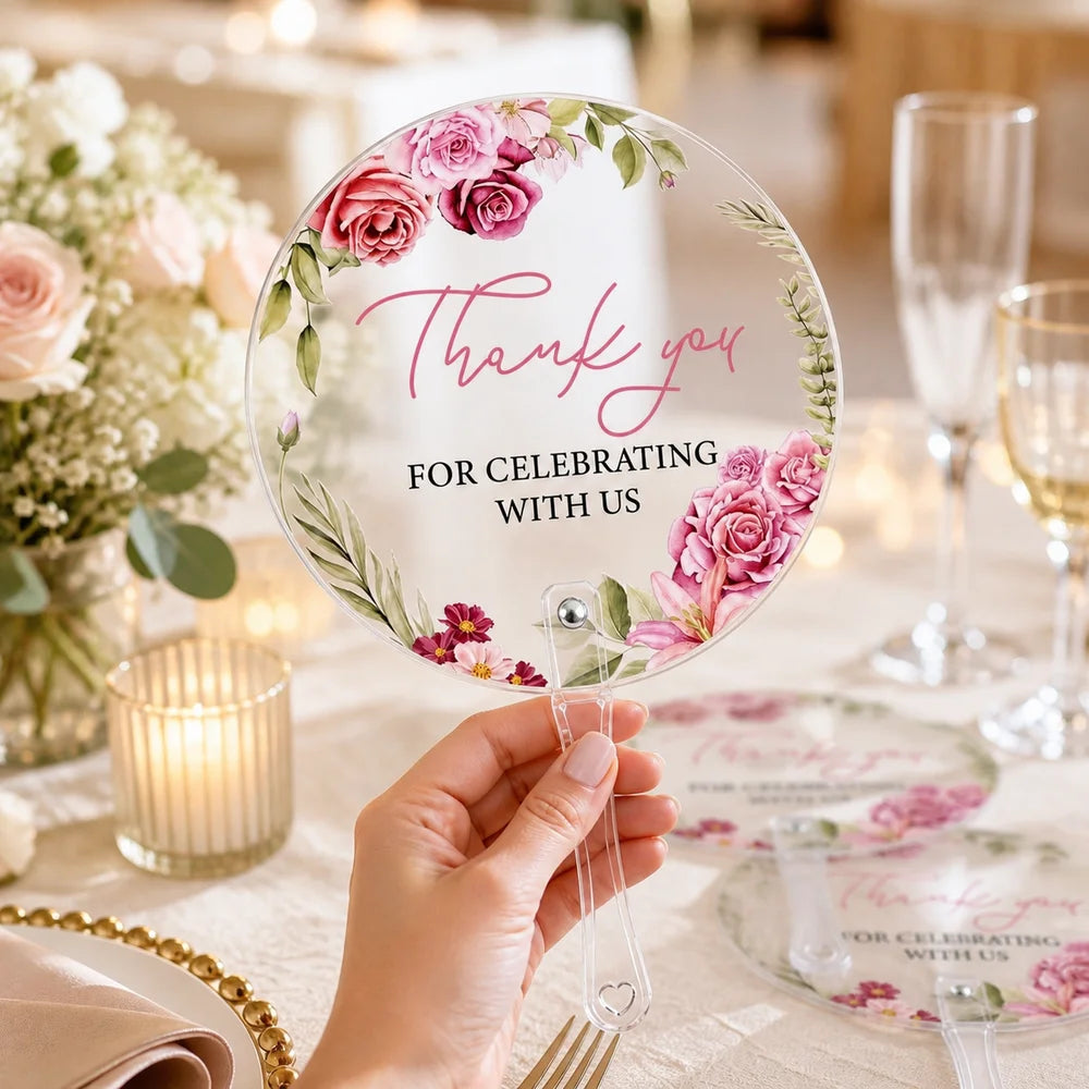 A hand holds a clear glass plate with pink floral designs and the words Thank you for celebrating with us