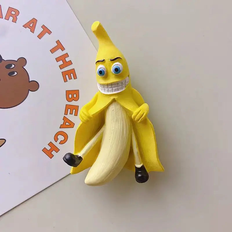 A yellow banana fruit fridge magnet with a wide, smiling mouth and white teeth is shown next to text that reads 'AR AT THE BE