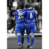 Two soccer players in blue jerseys stand side by side on a field.