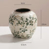 A white ceramic vase with green floral patterns and a dark rim, shown against a light background.