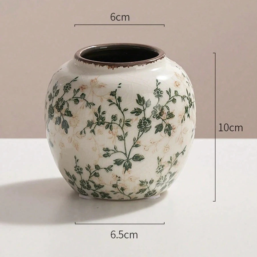 A white ceramic vase with green floral patterns and a dark rim, shown against a light background.