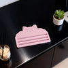 A pink cat face squeezer tool rests on a black surface next to a small potted succulent plant.