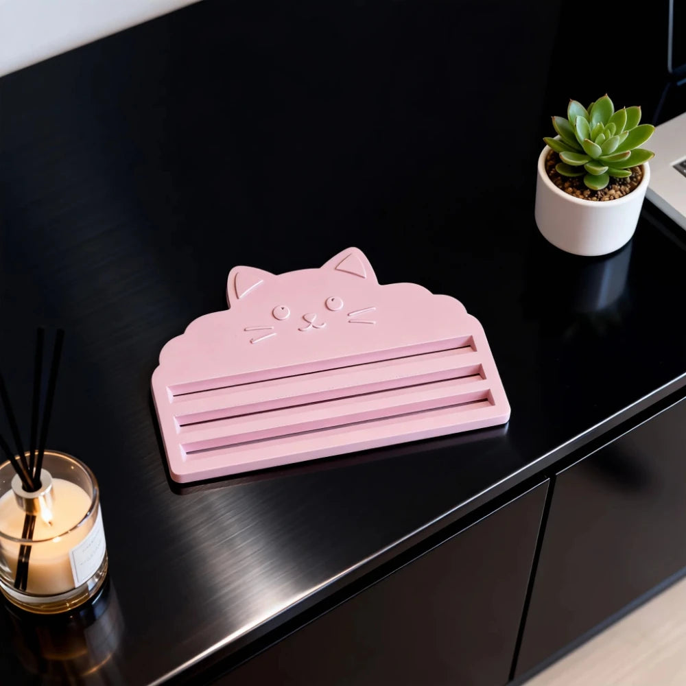 A pink cat face squeezer tool rests on a black surface next to a small potted succulent plant.