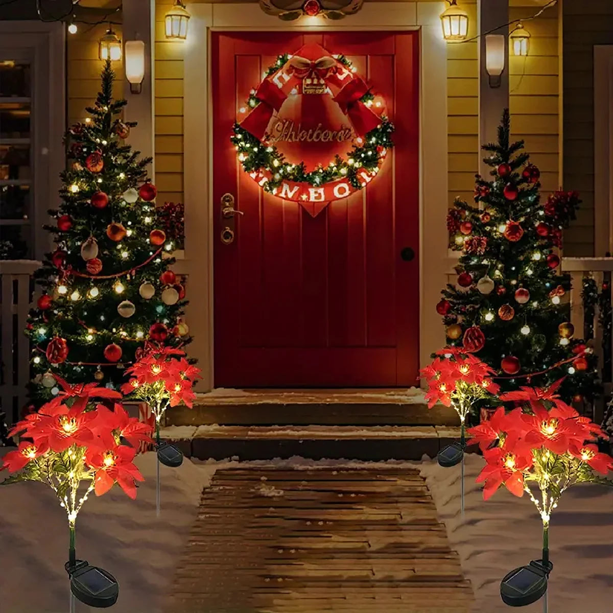 Red door decorated with a wreath and surrounded by glowing red poinsettia garden lights in front of a house.