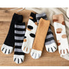 A set of plush socks featuring various cat paw print patterns in black, white, gray, and tan on a wooden surface.