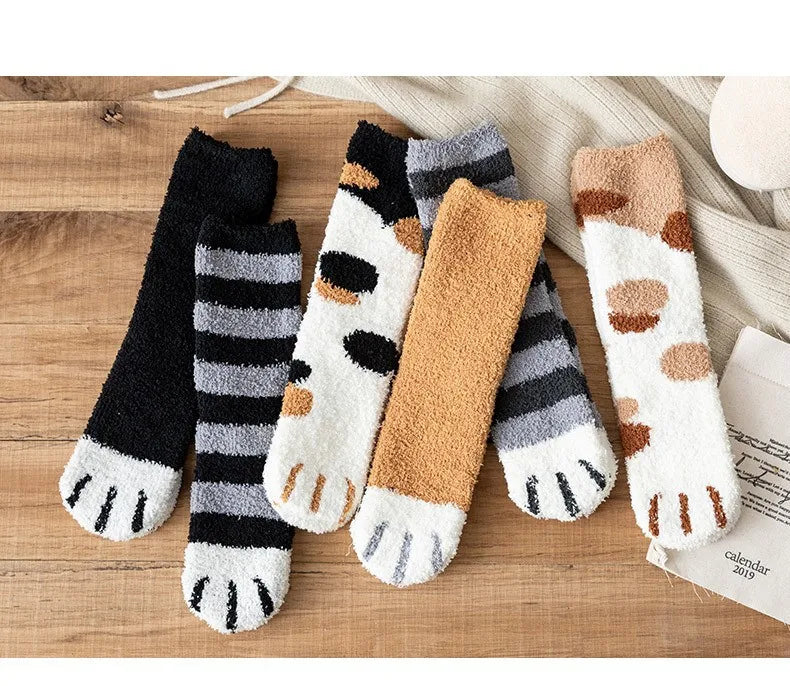 A set of plush socks featuring various cat paw print patterns in black, white, gray, and tan on a wooden surface.