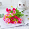 A bouquet of vibrant pink and magenta artificial daisy flowers displayed on an open book next to a cute ceramic teapot.