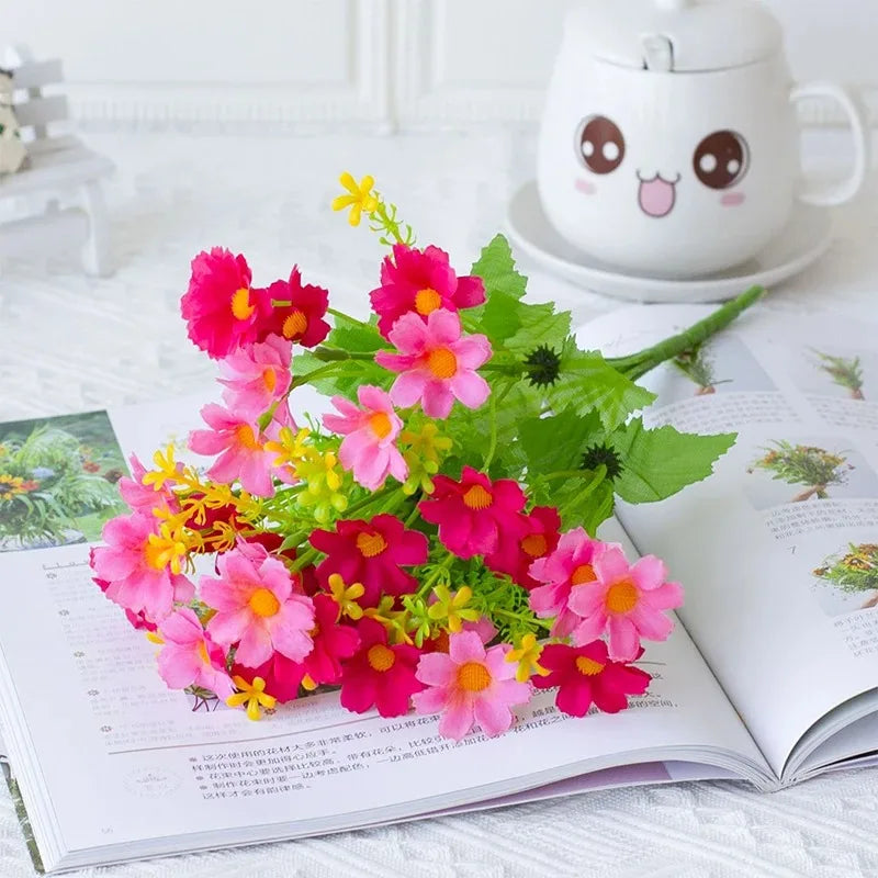 A bouquet of vibrant pink and magenta artificial daisy flowers displayed on an open book next to a cute ceramic teapot.
