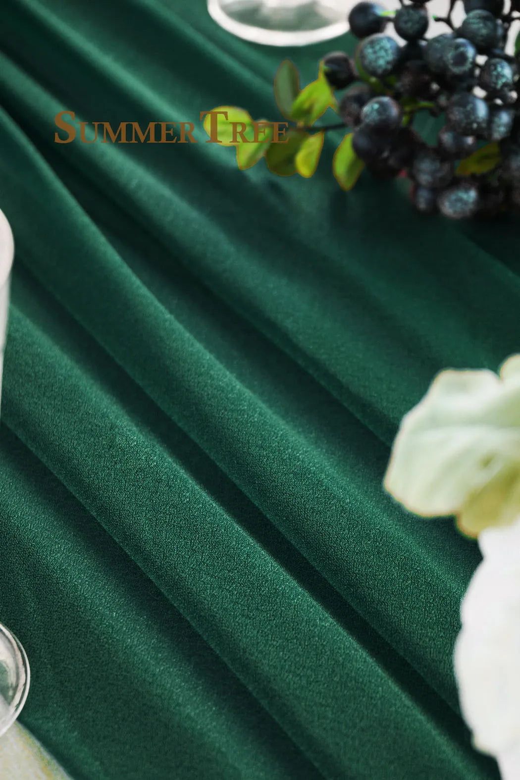 Deep emerald green chiffon fabric draped elegantly with dark berries and light floral accents.