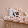 Pink sakura flower garland displayed on a wooden mantelpiece with books.