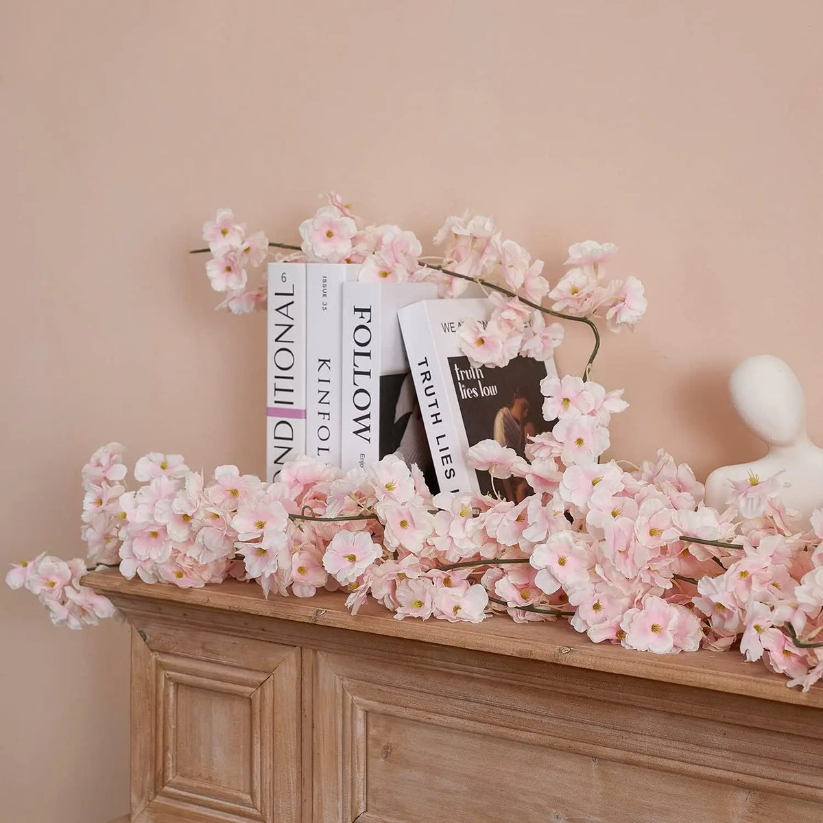 Pink sakura flower garland displayed on a wooden mantelpiece with books.