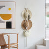A macrame hat organizer with a wooden dowel is displayed as a boho wall hanging on a white wall.