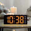 An orange digital alarm clock displaying 10:38 on a wooden surface with soft lighting in the background.