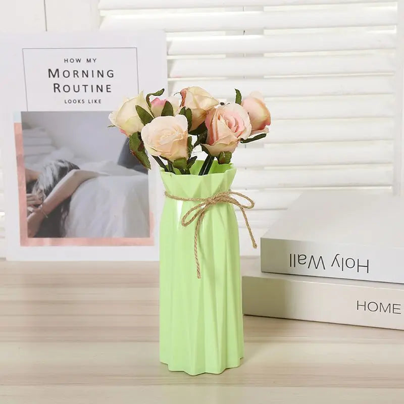 A light green plastic vase holds a bouquet of pink roses on a wooden surface.