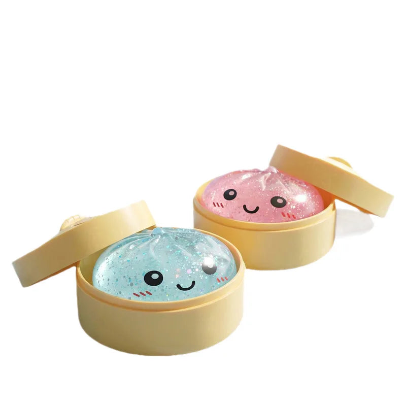 A set of two squishy toys shaped like dumplings, one pink and one blue, in light yellow containers.