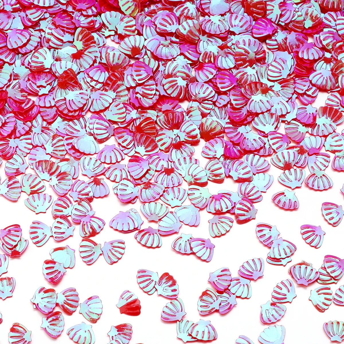 A close-up of pink and red sea shell PVC sequins scattered across a white background for nail art and craft decoration.