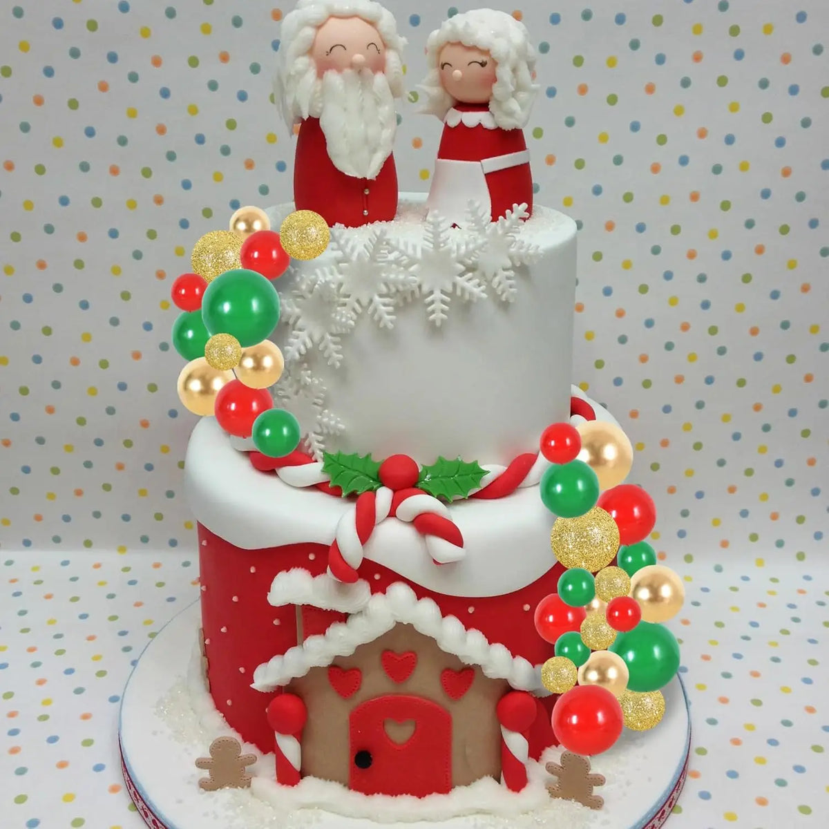 A tiered cake featuring a red house design and white figures with beards and crowns, decorated with colorful foam balls.