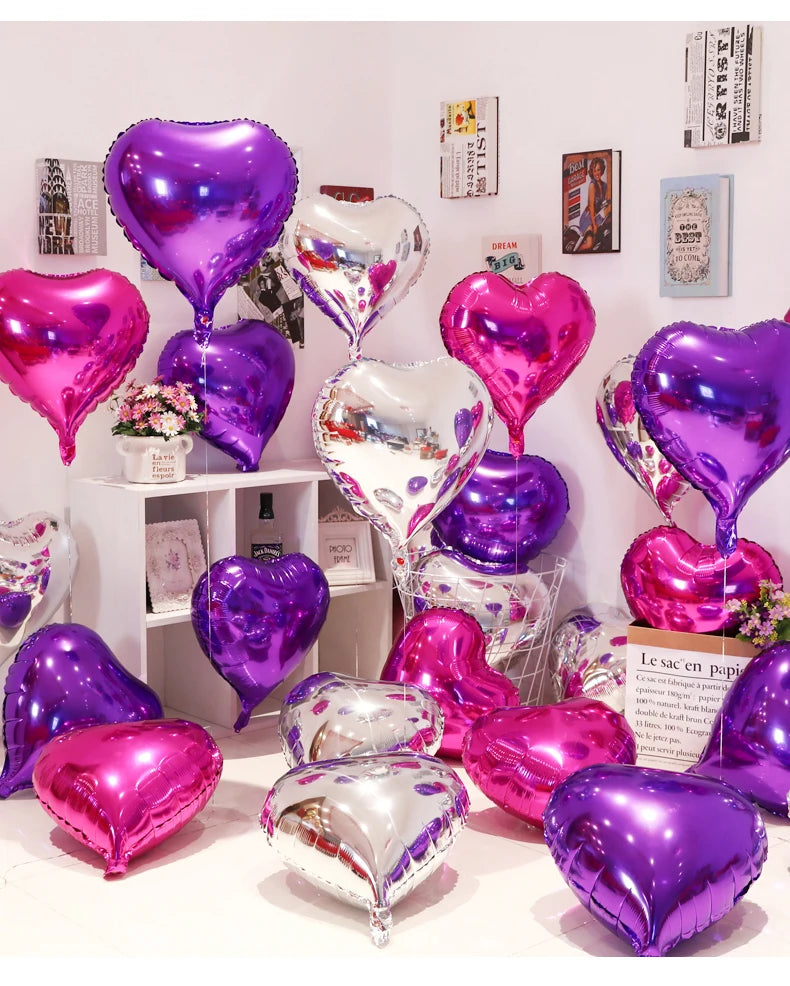 A collection of iridescent and metallic foil heart balloons in various shades of purple and pink displayed on a white shelf.